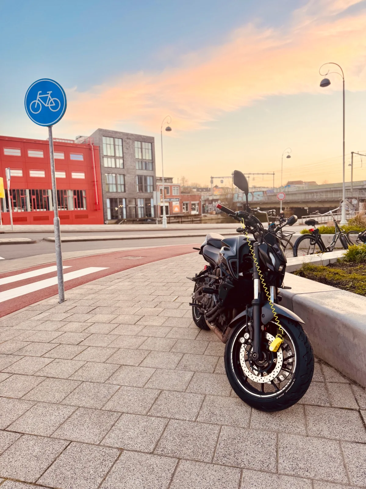 Black Yamaha MT-07 parked near a bicycle lane sign on an Amsterdam street at sunset