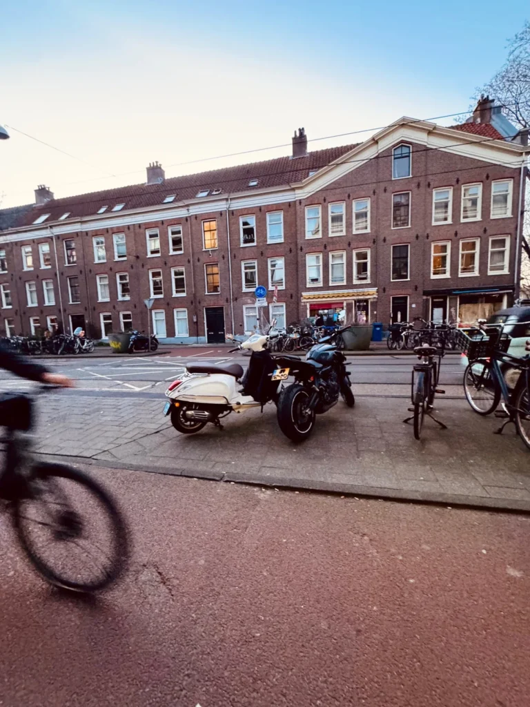 Motorcycle and scooter parked beside a street with a cyclist passing in traffic