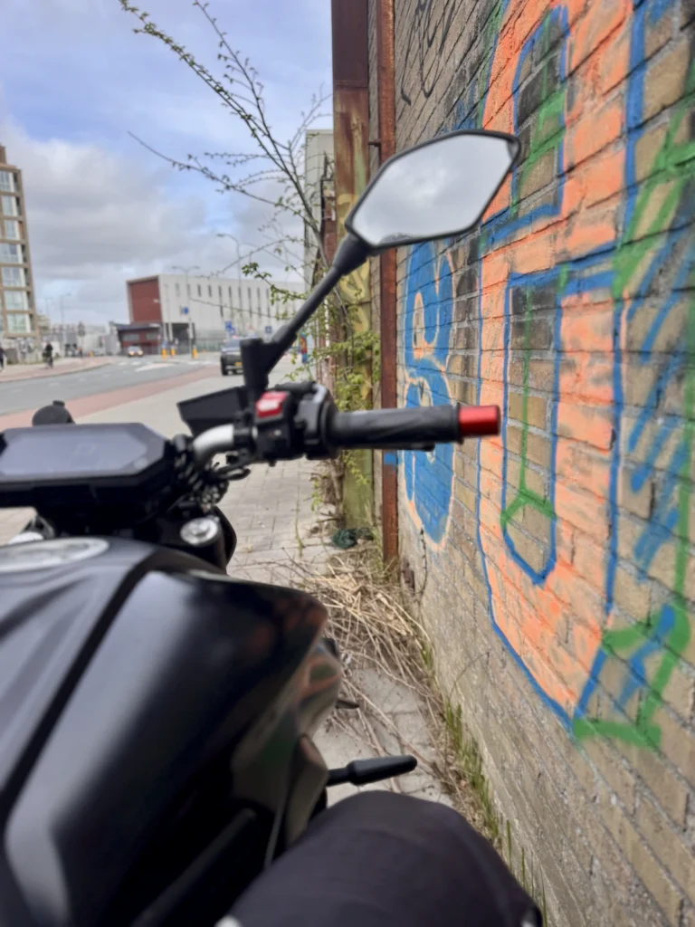Handlebar view beside a rough roadside wall showing careful line choice near road edges