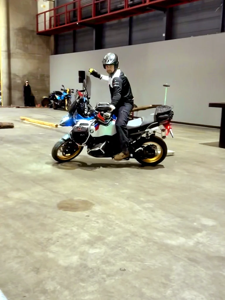 Rider practicing indoor slow motorcycle control with one hand during balance training